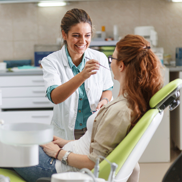 A dentist in a white coat smiles warmly while examining a patient's teeth in a Texas dental office.