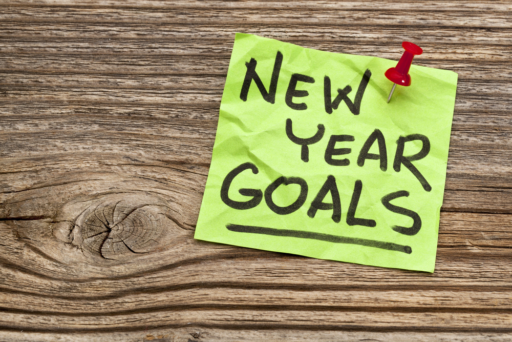 green sticky note that says "NEW YEAR GOALS" pinned on wooden wall