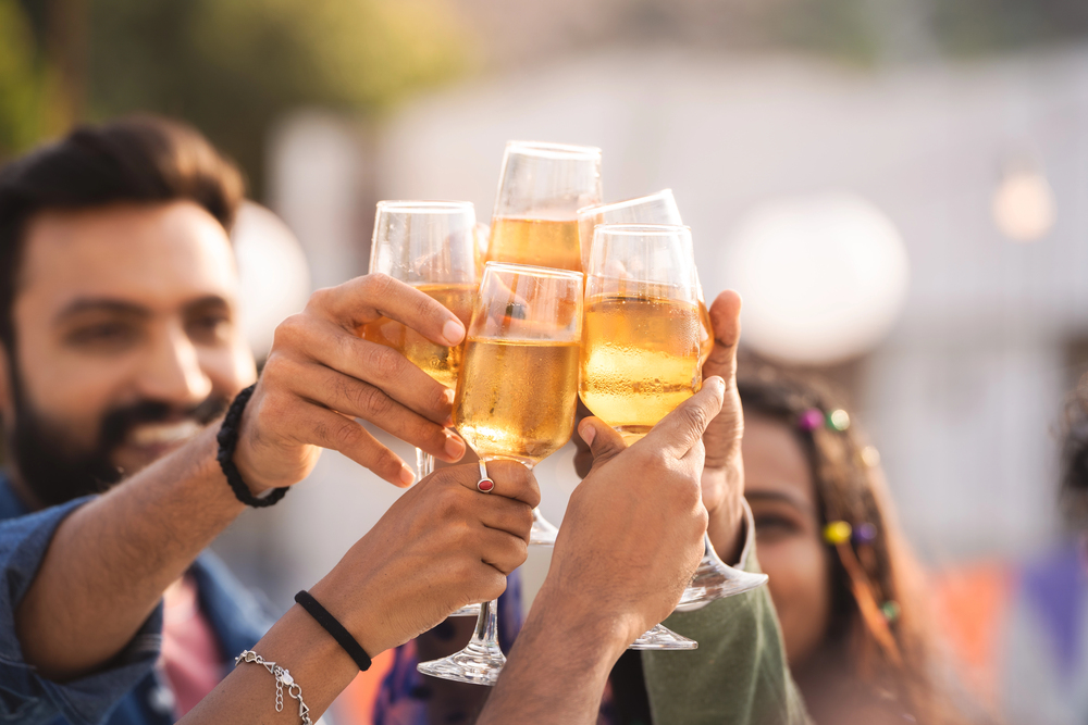 A group of people clinks glasses filled with a golden beverage, celebrating together outdoors.