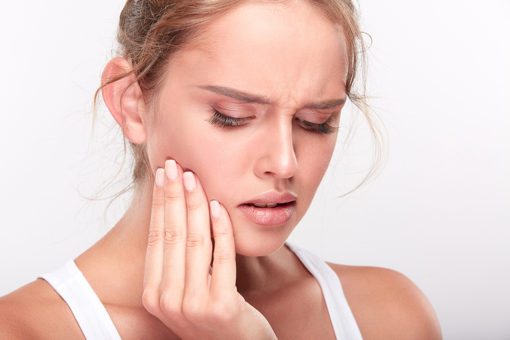 A woman touching her cheek with a pained expression, possibly experiencing discomfort from a toothache or jaw issue that may require a root canal.