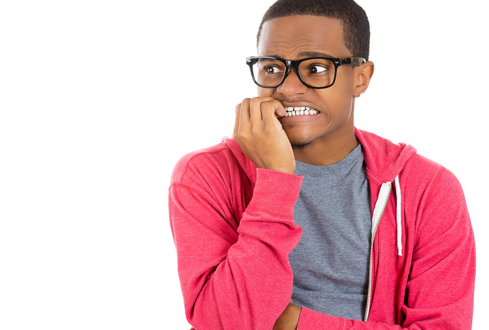 A person wearing glasses and a red hoodie bites their nails and looks anxious, standing against a white background.
